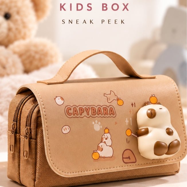 A tan canvas kids box or pencil case with a top handle, featuring cute cartoon animal illustrations, the text 'CAPYBARA', and a large 3D panda charm on the front. The image has a soft, blurred background with a teddy bear and includes the text 'KIDS BOX' and 'SNEAK PEEK' at the top.